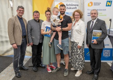 (v.l.n.r.): Stefan Haertl (Geschäftsführer Schönere Zukunft), Pfarrer Marius Claudiu Zediu, Csilla Klein und Peter Schmidt mit Nachwuchs, Wohnbau-Landesrätin Christiane Teschl-Hofmeister und Bürgermeister Alois Zetsch.